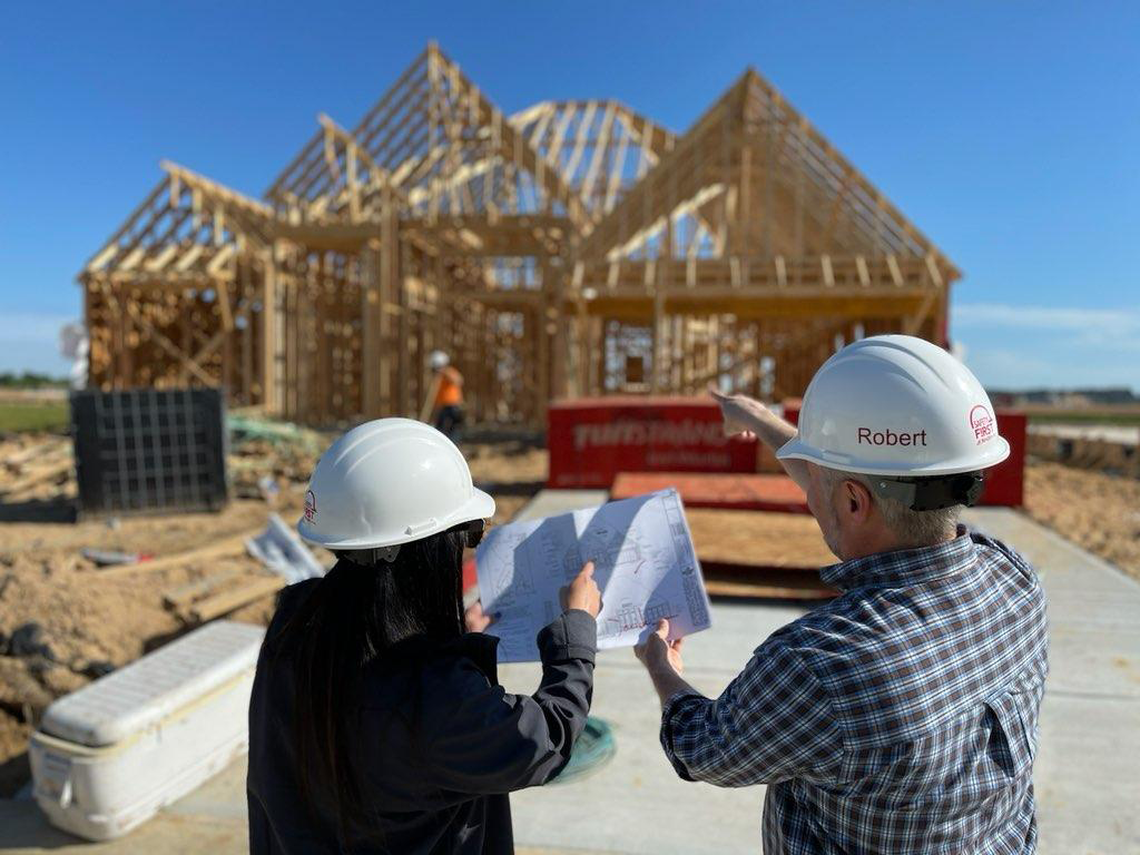 Two Beazer employees standing in front of a home under framing