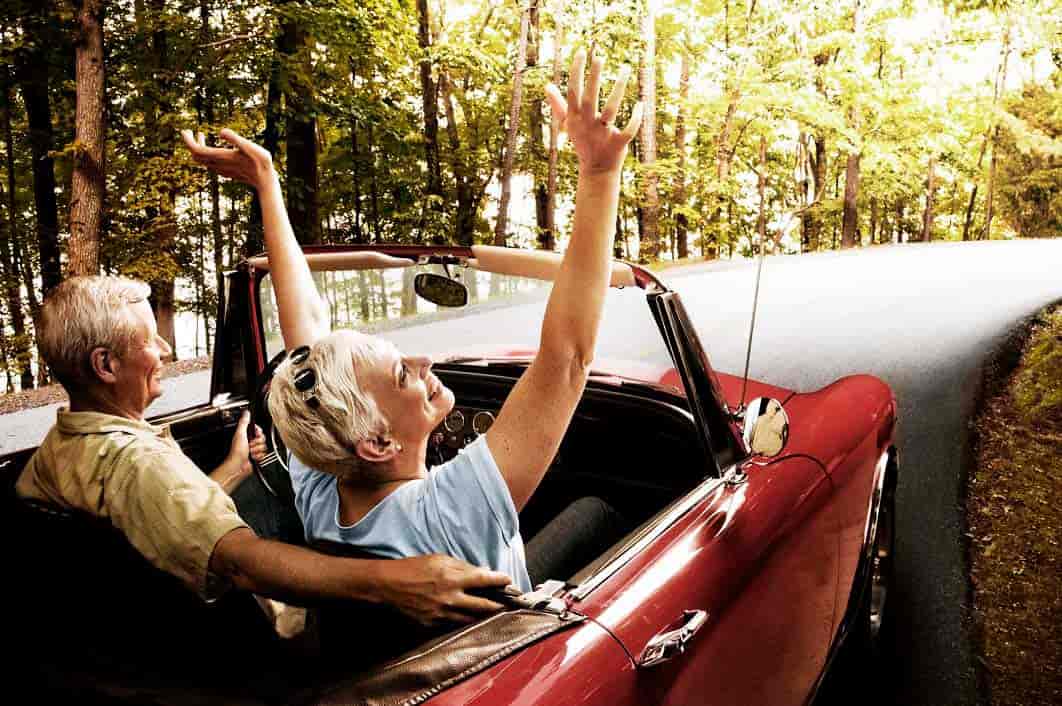 couple driving down a wooded road in a red convertible